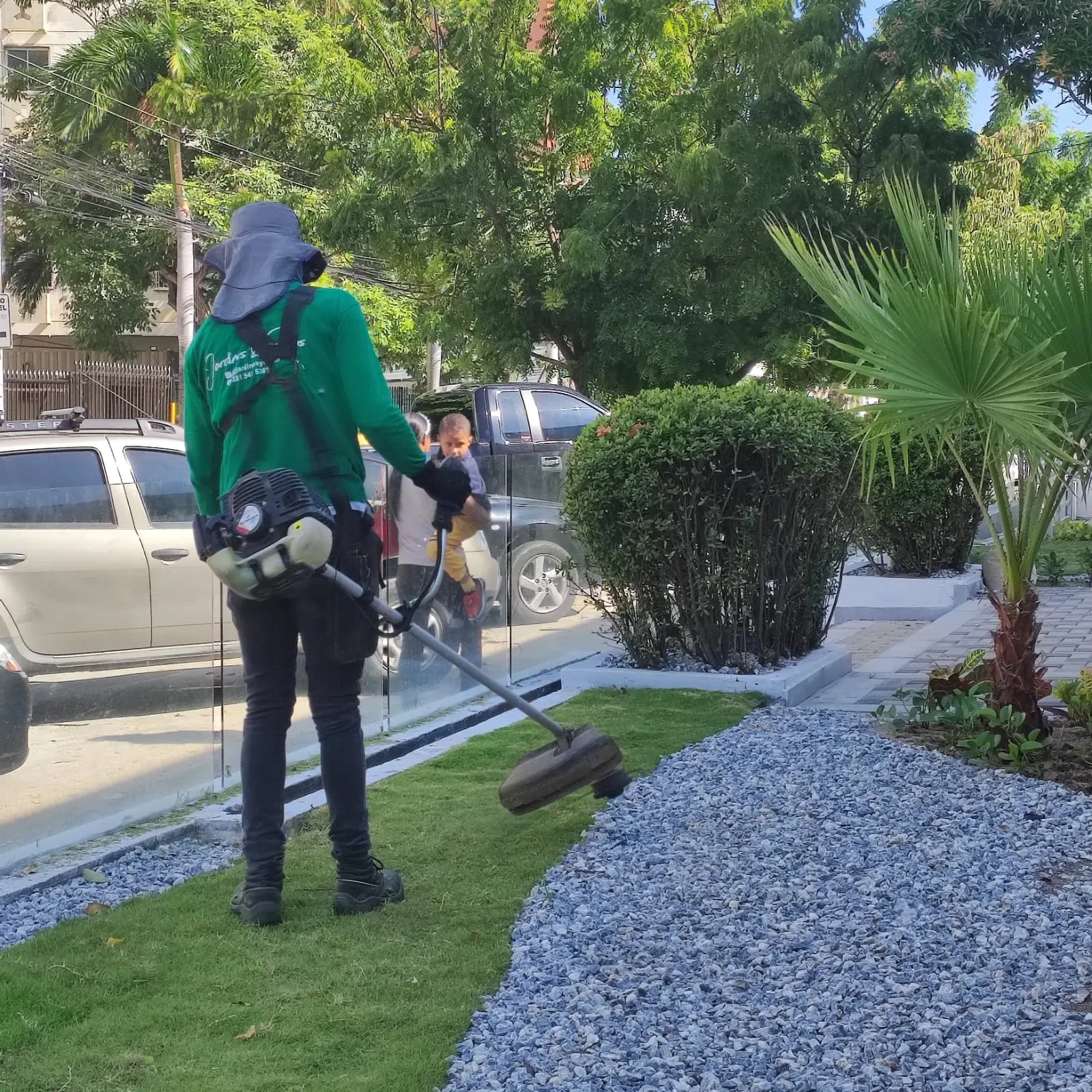 Jardinero cortando grama natural junto a un sendero de triturado gris y palmas en Barranquilla