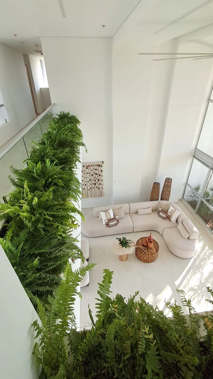 Ambientación interior en doble altura con jardinera lineal suspendida de helechos en mezzanine
