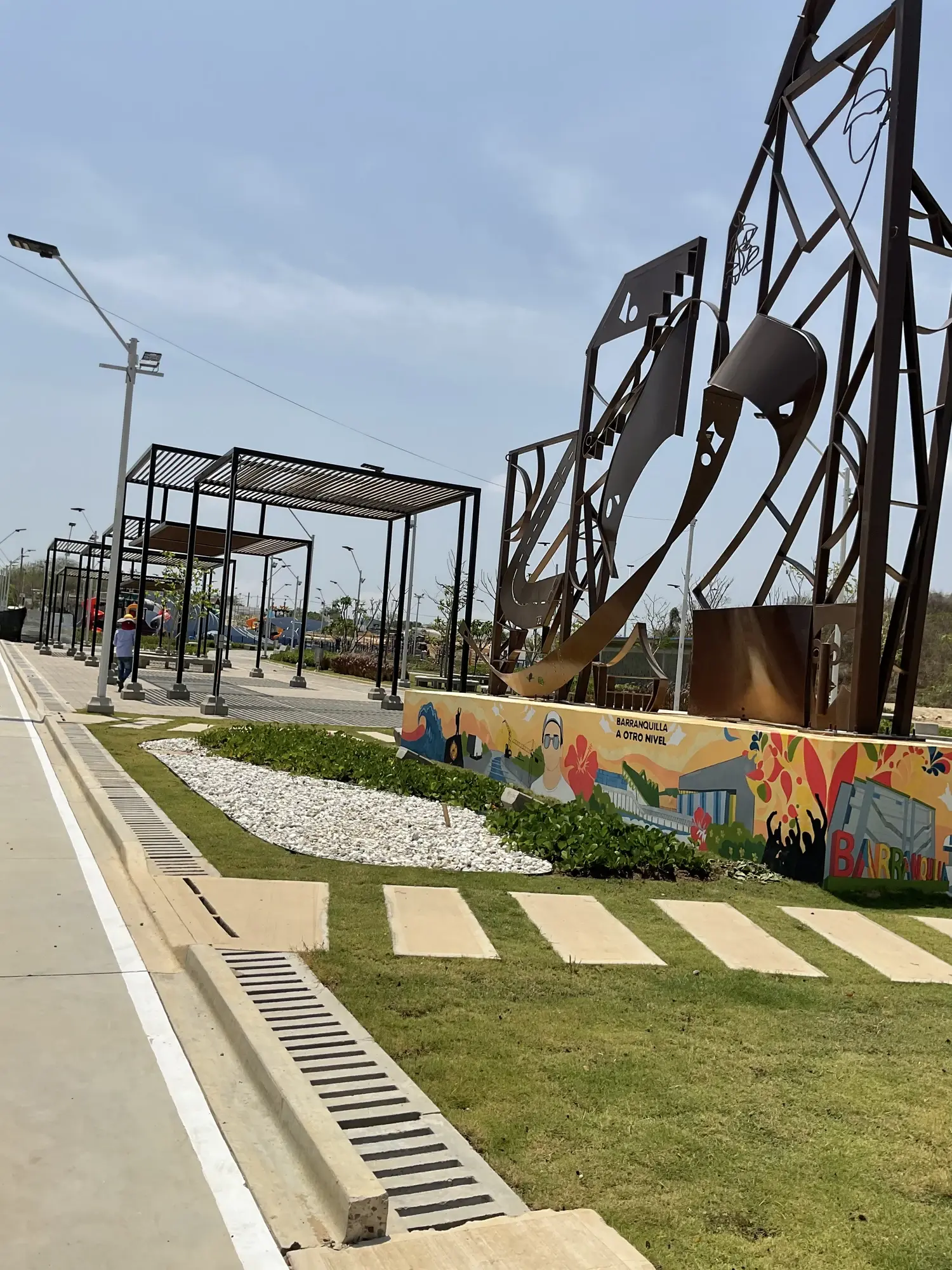 Plazoleta con pérgolas metálicas, escultura monumental, mural artístico y senderos en piedra