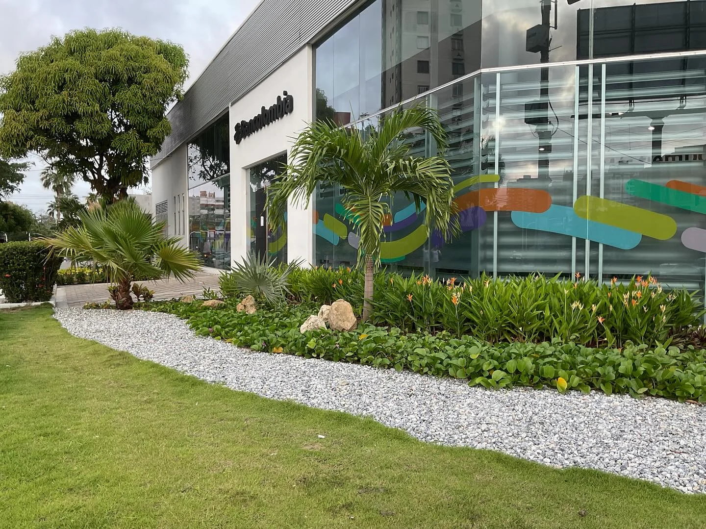 Acceso peatonal en adoquines, palmas Manila y heliconias en flor